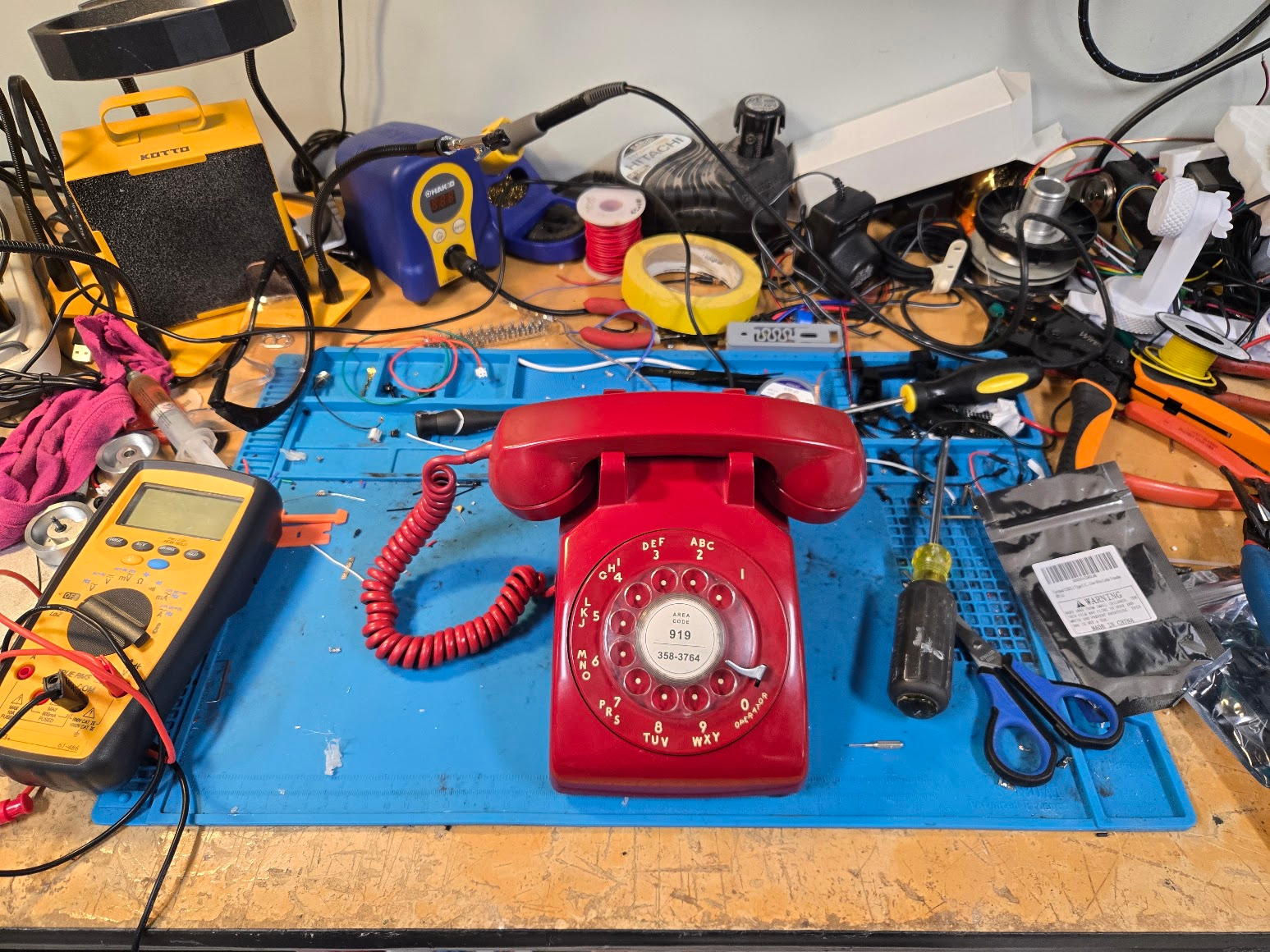 Completed red RotaryCell telephone centered on an electronics workbench